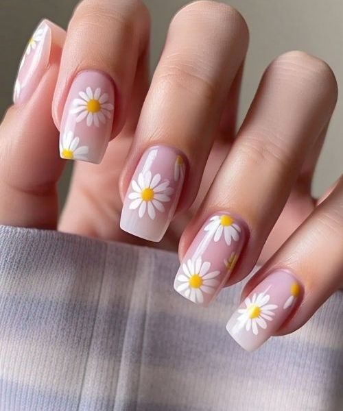 1. A Beautifully Manicured Hand With Long Sleeves, Featuring Floral Spring Nails With A Pastel Pink Base And Delicate White Daisy Accents On Two Nails, Capturing A Soft And Charming Spring Vibe